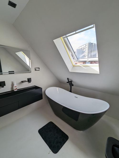 Loft bathroom with black freestanding bath, wall-mounted taps and roof window