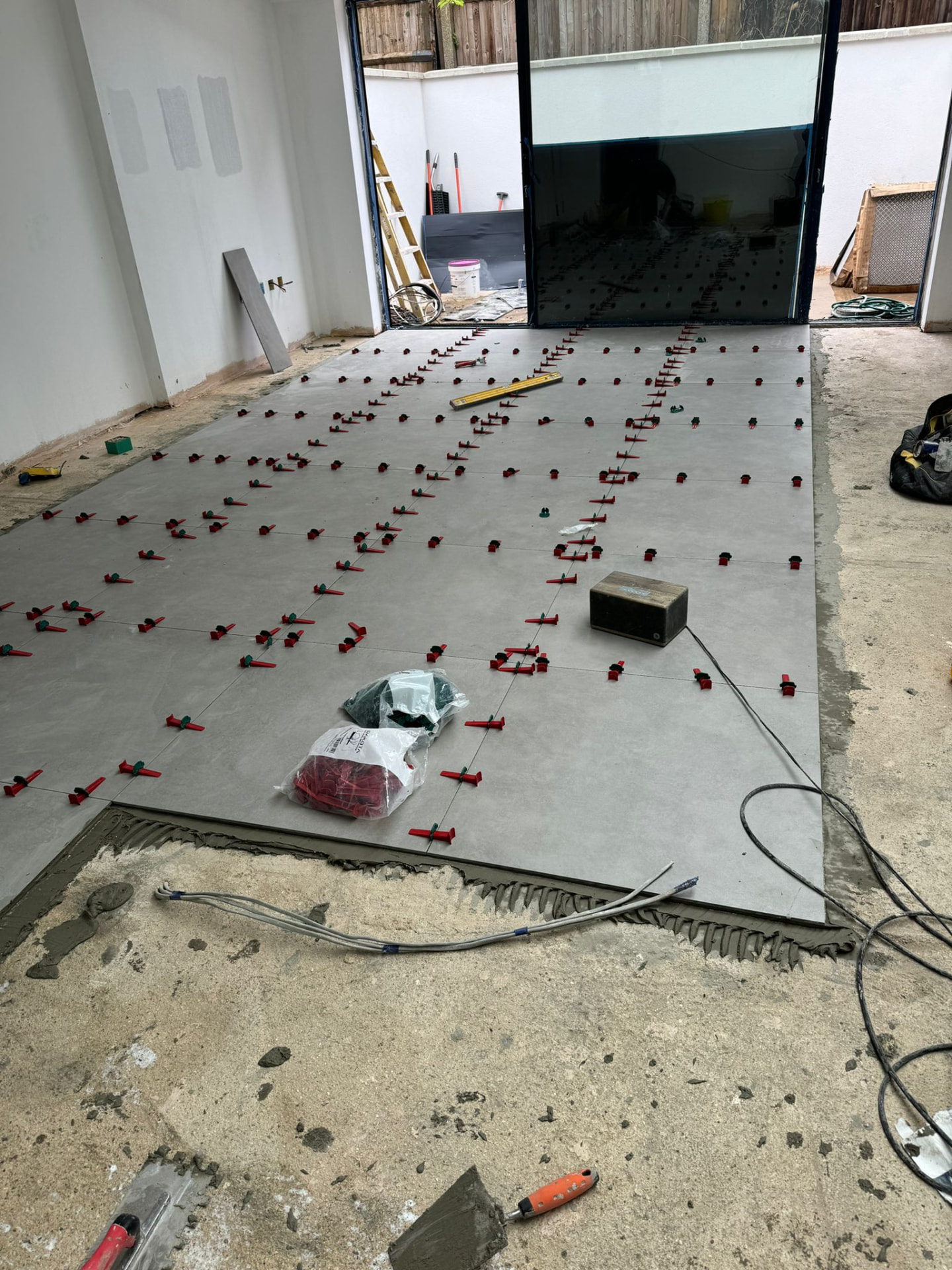 Large-format porcelain floor tiles being laid with a levelling system by the glazed doors